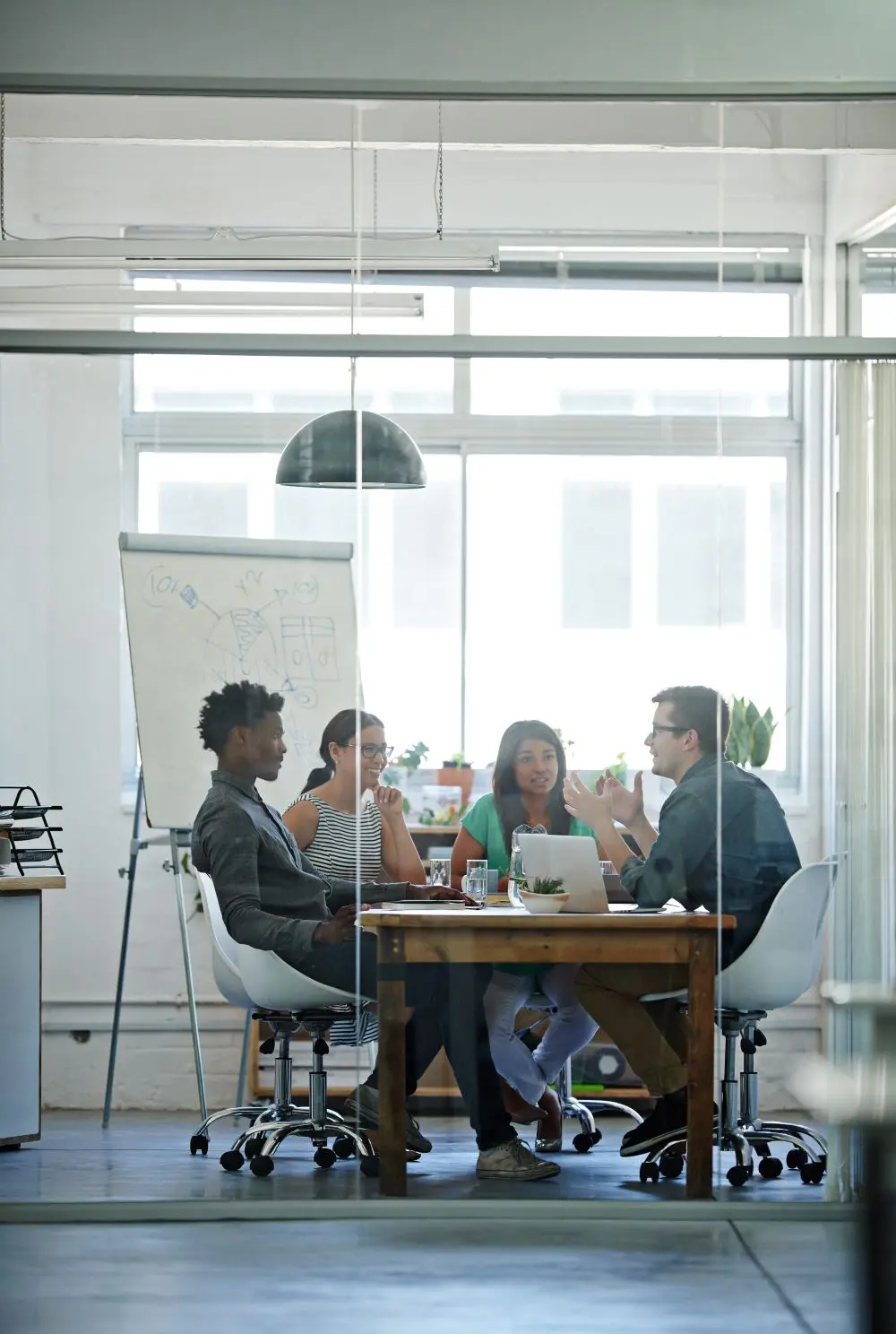 Group of four college students sitting around a table interacting with a whiteboard behind them